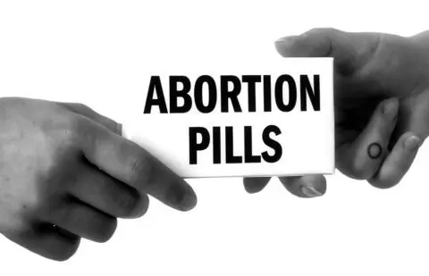 Two hands exchanging a box labeled Abortion Pills in black and white, highlighting phar...