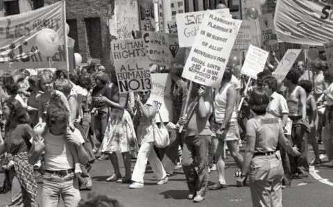 People marching with signs for human and gay rights in a protest, advocating for equali...