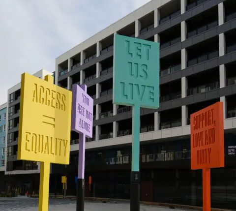 Colorful protest signs outside a modern building, reading Access = Equality and Let Us ...