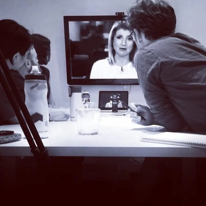 Team in meeting room watching a video call on a monitor while discussing and taking not...