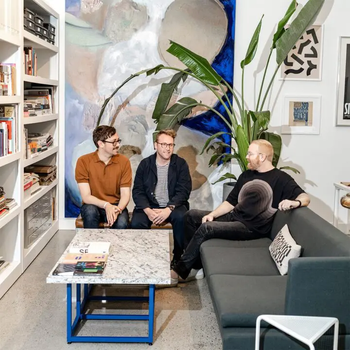 Three people having a casual meeting in a stylish office with art and plants, sitting o...