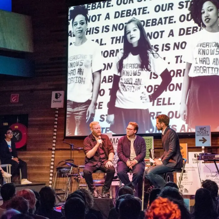 Panel discussion on stage with large abortion rights image display in background, featu...