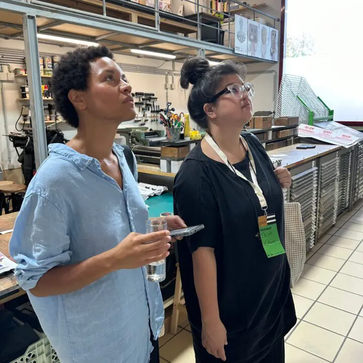 Two people observing a creative workspace, surrounded by art supplies and posters.