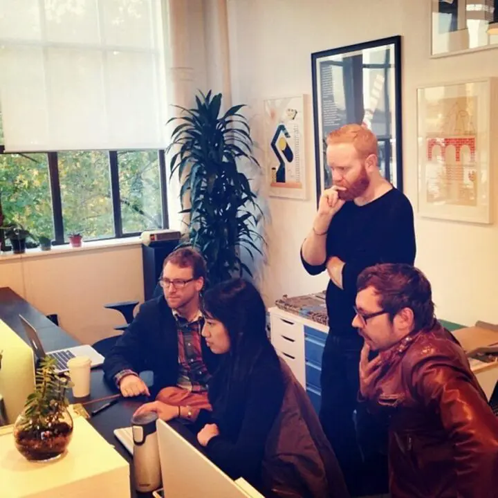 Team collaborating on a project in a modern office space, with laptops and a large wind...