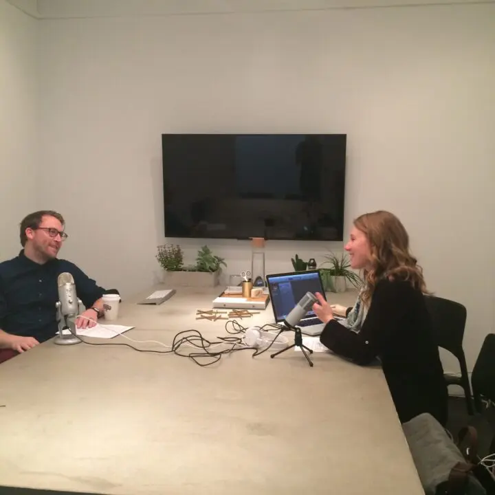 Two people recording a podcast in a modern office with microphones and laptop on a table.