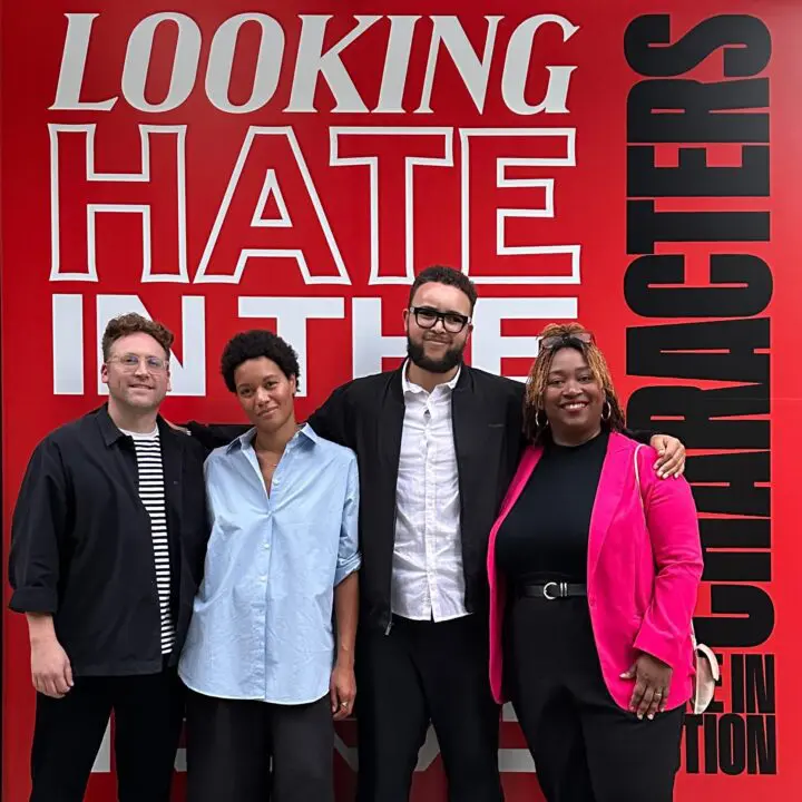 Group standing in front of a bold graphic on 'hate' theme, posing confidently. Diversit...