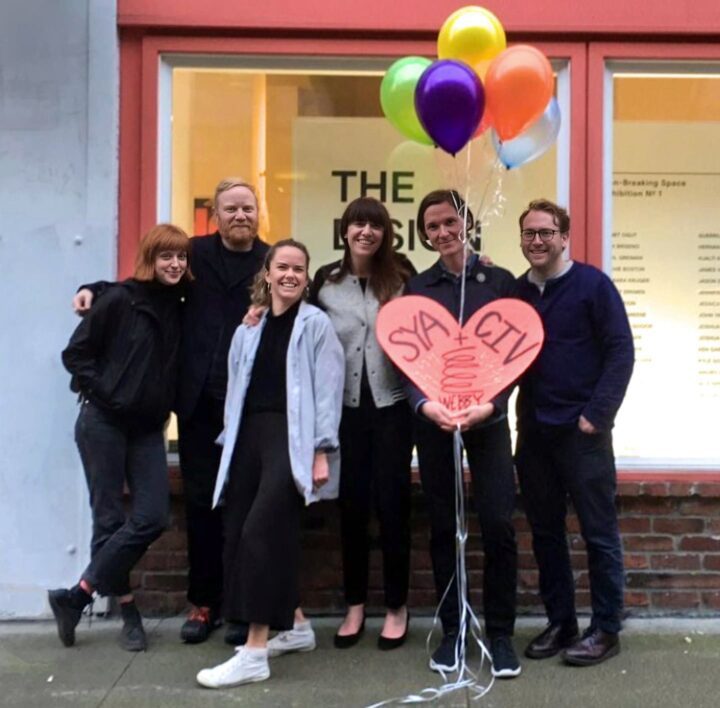 Group celebration with colorful balloons and heart-shaped sign in front of a storefront...