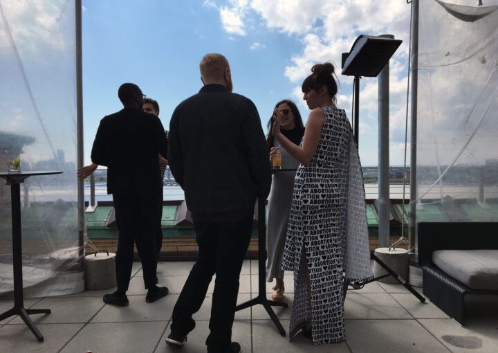People socializing at a rooftop gathering under a blue sky, with a focus on casual conv...