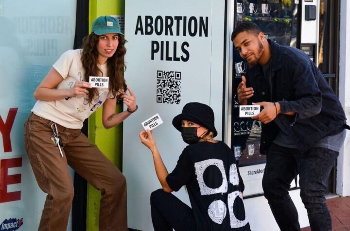 People holding signs reading Abortion Pills next to a vending machine offering abortion...