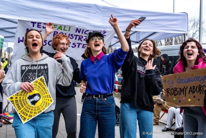 Group of people at a protest, smiling and holding signs under a tent. Activism and comm...