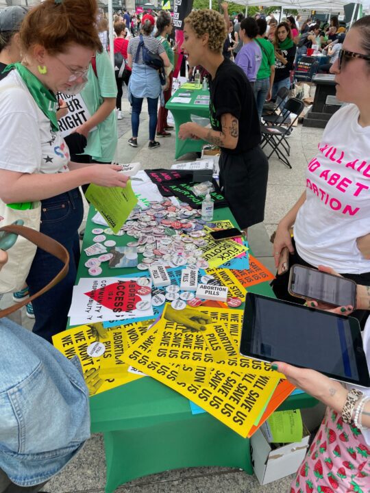 People engaging at a reproductive rights event, browsing advocacy buttons and signs pro...