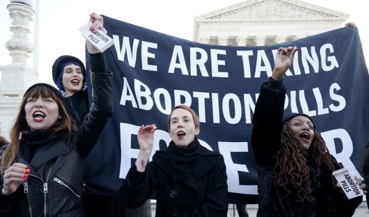 Protesters holding We are taking abortion pills banner in front of a government buildin...