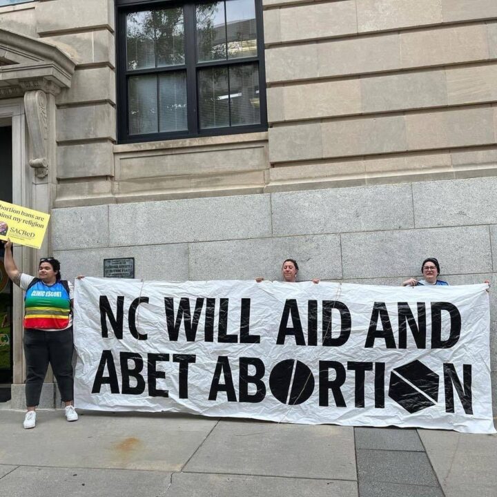 Protesters holding a banner saying NC will aid and abet abortion outside a building.