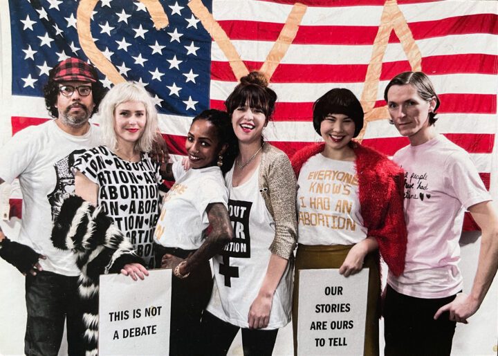 Diverse group standing with pro-choice signs in front of an American flag, advocating f...
