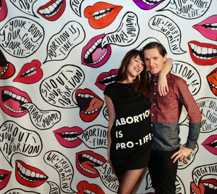 People in front of a vibrant mural with pro-choice messages and bold red lips, advocati...