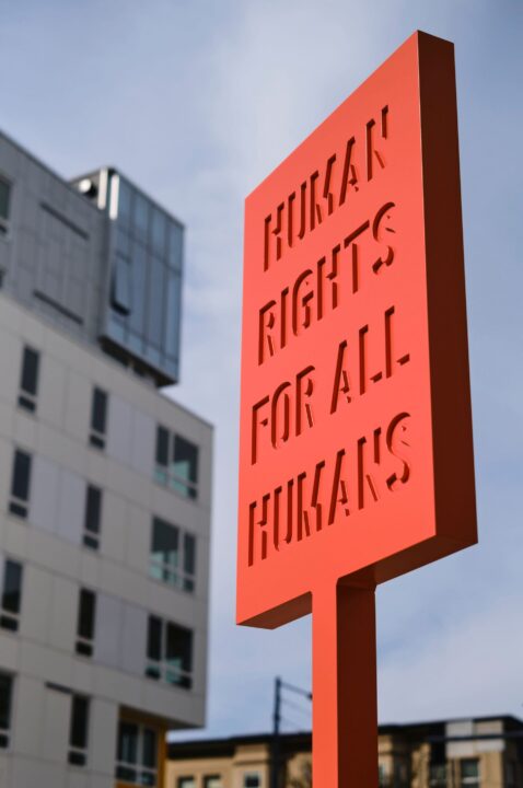 Red sign with the message Human Rights for All Humans in front of modern buildings, hig...