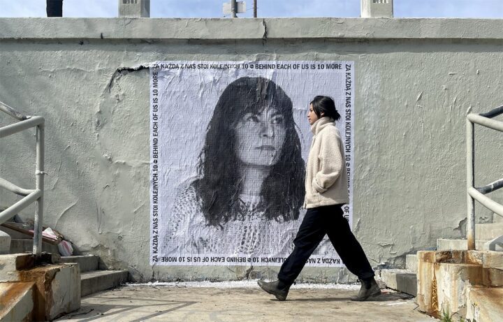 Woman walking past black-and-white mural with text Behind Each of Us is 10 More on urba...