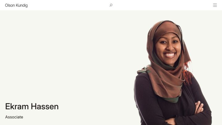 Smiling professional in brown hijab, labeled Associate at Olson Kundig, standing agains...