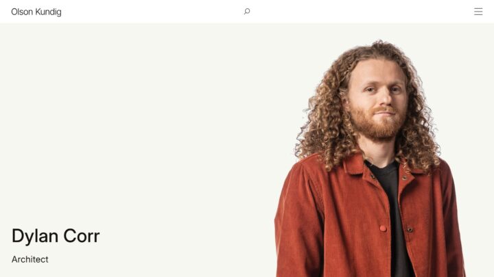 Portrait of a man with curly hair and a red jacket on a minimalist background.