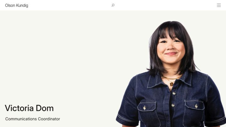 Portrait of a woman in a denim shirt with short black hair, smiling against a light bac...