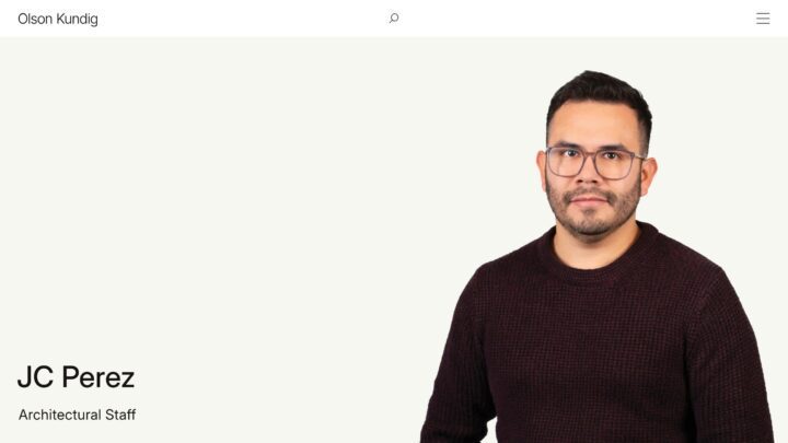 Man in glasses wearing a dark sweater, standing against a light background with JC Pere...