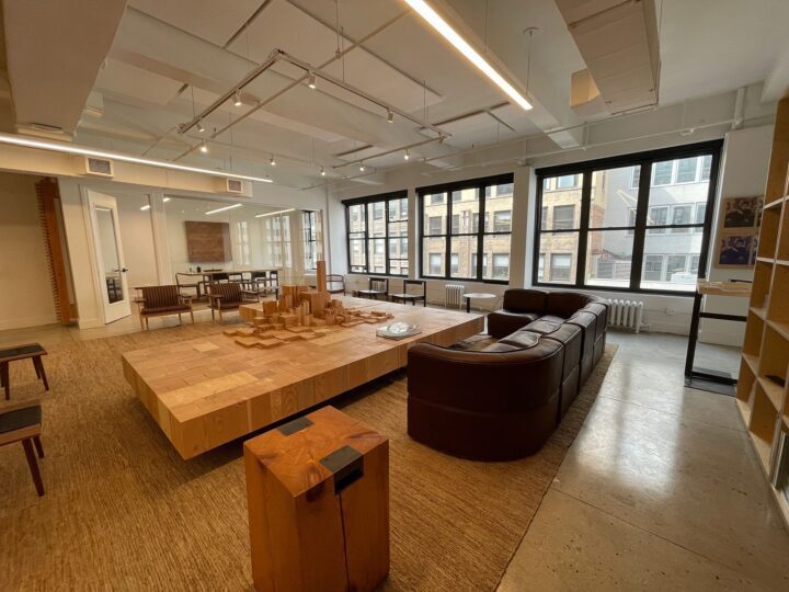 Modern office space with large windows, brown leather couch, wooden tables, and models,...