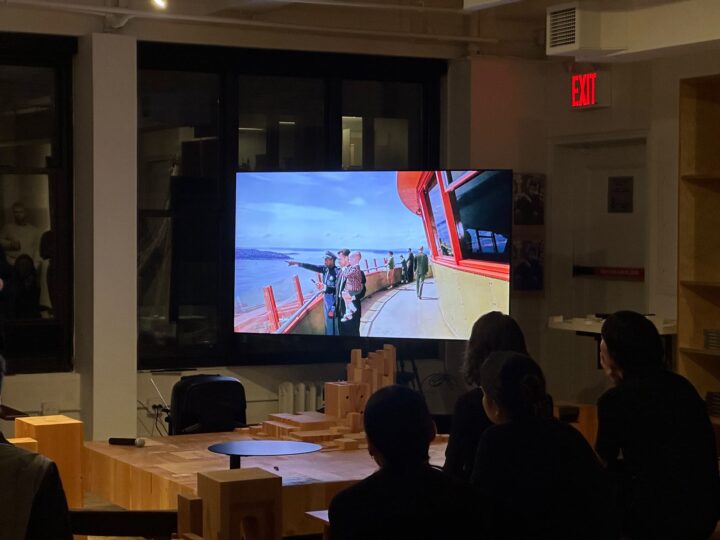 People watching a movie in a dimly lit room, with a large screen displaying a scenic view.
