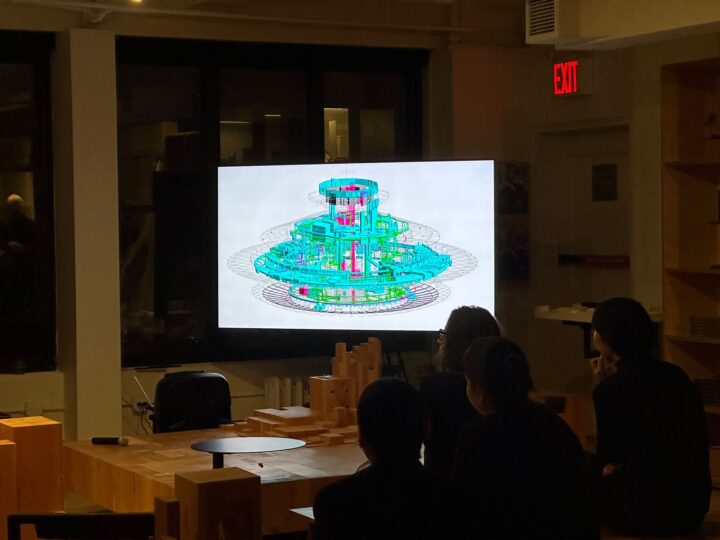People watching a 3D architectural model on a presentation screen in a dimly lit room.