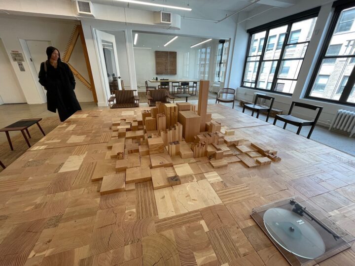 Wooden city model on a large table inside a bright, modern office space with a woman ob...