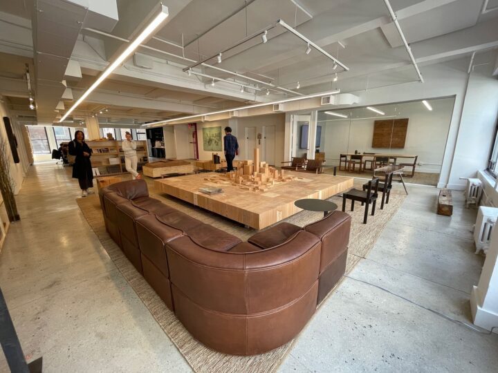 Modern office lounge with a wooden table, brown leather sofa, and people interacting in...