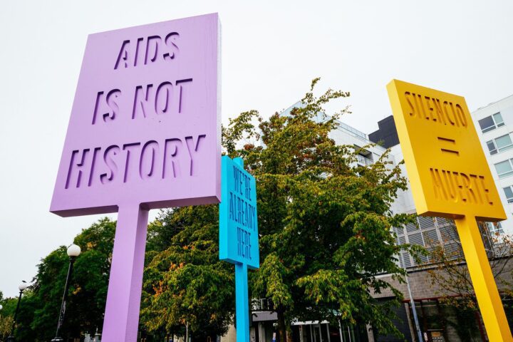 Colorful protest signs with messages about AIDS and silence in an urban setting, surrou...