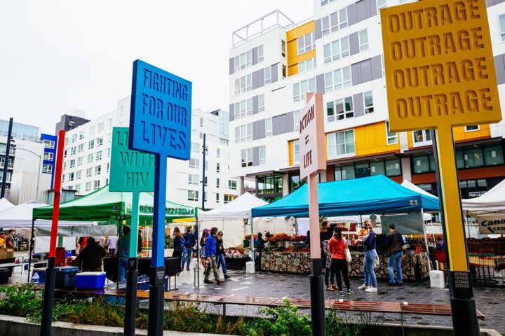 Colorful protest signs at a lively outdoor market, highlighting social issues against a...