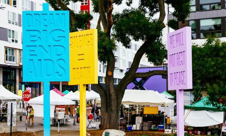 Colorful signs promoting AIDS awareness near a local market, with messages: Dream Big E...