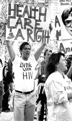 Protester holding Health Care is a Right sign at rally with Living with HIV shirt, advocating for healthcare rights.
