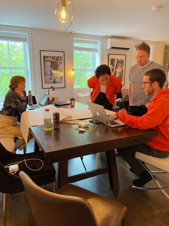 Civilization team collaborating around a table with laptops and documents in a bright room.