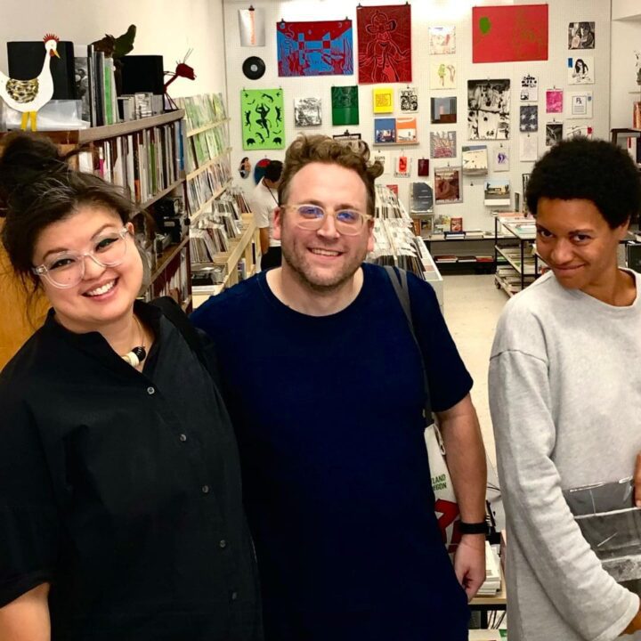 Trish Chua, Michael Ellsworth, and Raya Leary smiling in a colorful bookstore in Porto Portugal filled with art and books.