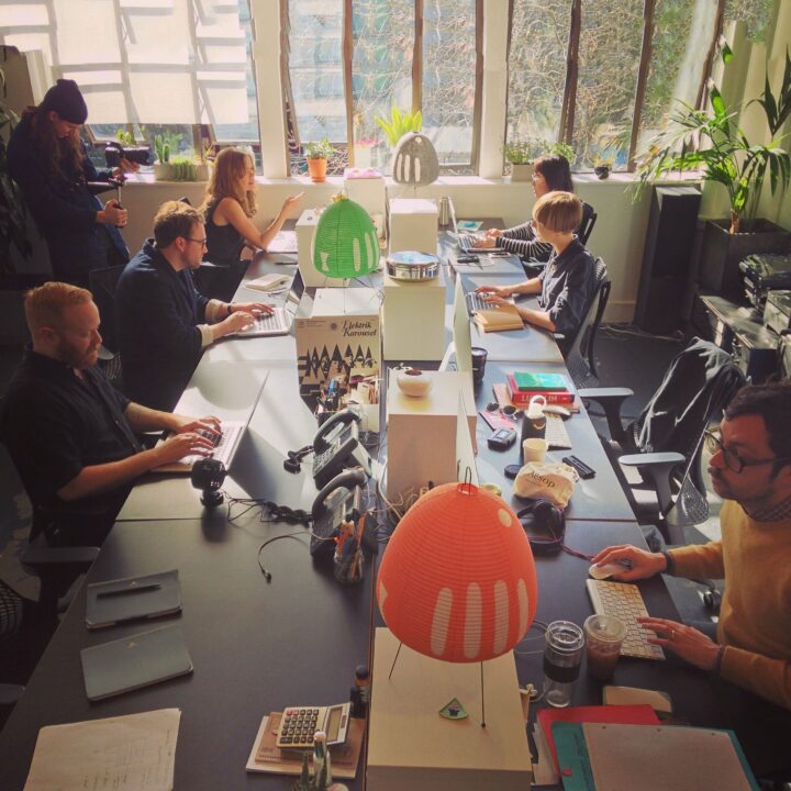 Our first office space in 2012 with Civilization working at desks, laptops open, natural light, indoor plants, collaborative workspace.