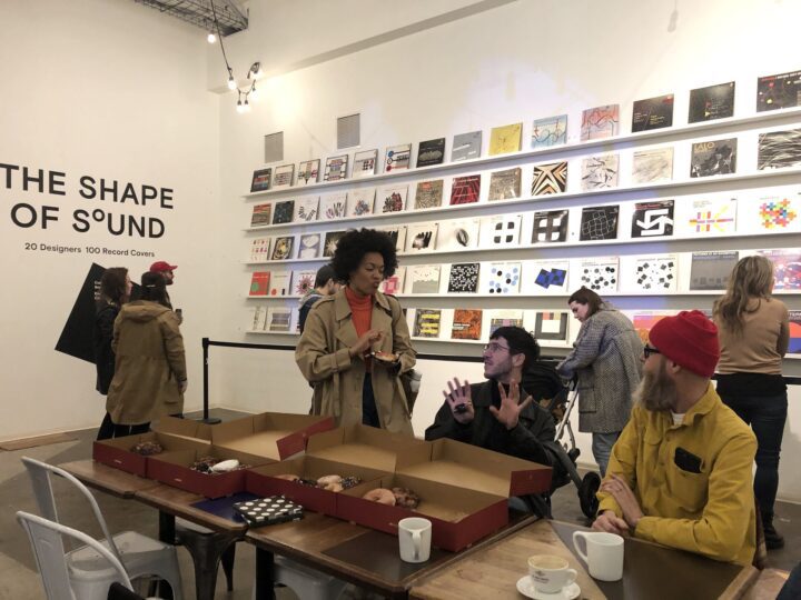 People enjoying coffee and examining creative record covers at The Shape of Sound gallery display.