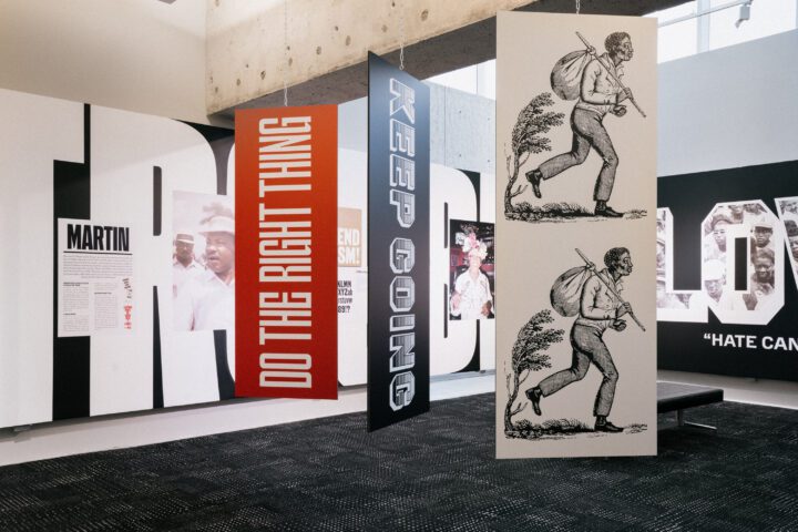 Exhibition with hanging signs: DO THE RIGHT THING, KEEP GOING, and illustrations of a m...