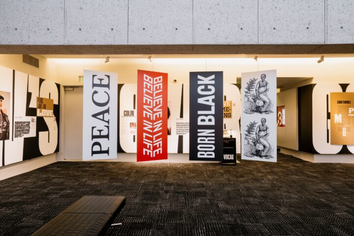 Art exhibit with banners saying PEACE, BELIEVE IN LIFE, BORN BLACK, and historic illust...