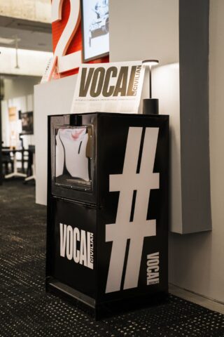 Black and white magazine stand with Vocal Civilian signage, featuring a hashtag symbol, in a modern office setting.