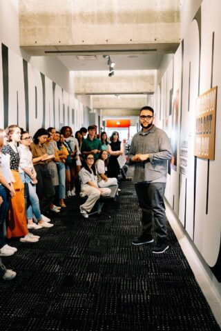 Group of students attentively listening to a speaker in a modern hallway presentation.