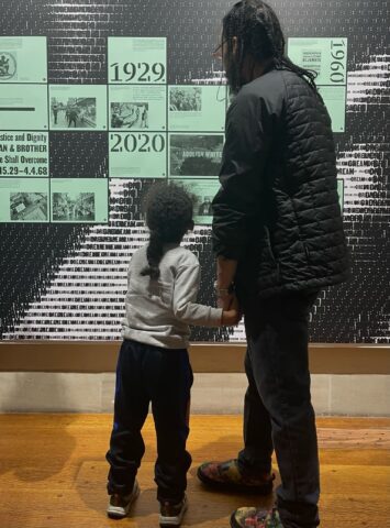 A man and child view a historical timeline display in a museum, highlighting significant years such as 1929 and 2020.