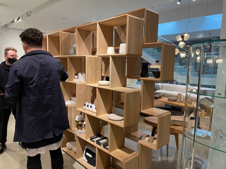 Modern showroom with wooden shelves displaying decor items, while two people converse n...