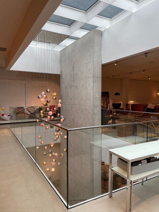 Modern interior with skylight, concrete column, and hanging spherical lights above glas...