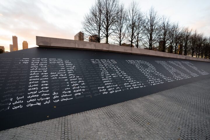 Memorial wall with names in various scripts at a park, bare trees in the background, ur...