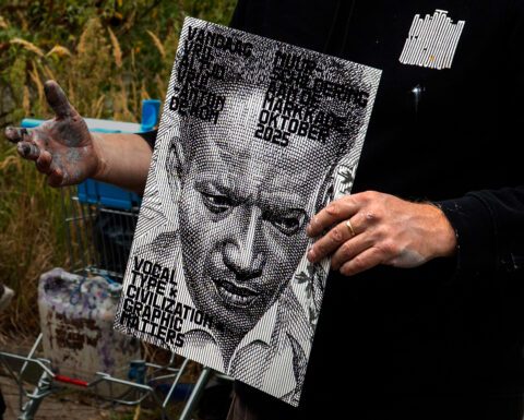 Person holding a detailed artwork print with a portrait and event text. Textured, monochrome design in an outdoor setting.