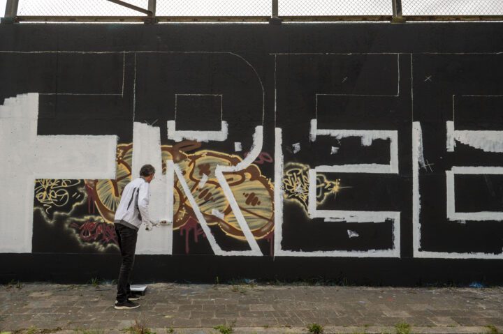 Artist painting large FREE graffiti on a black wall, adding white paint with a roller, ...