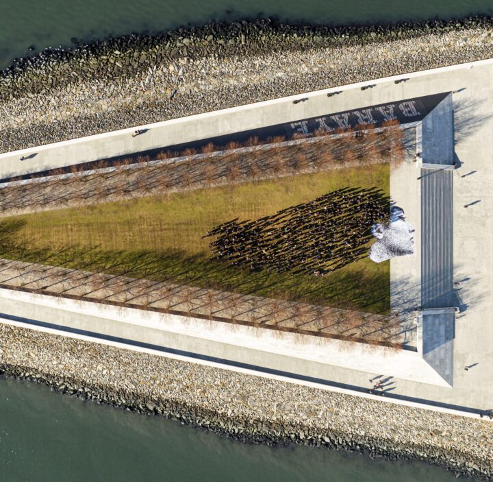 Aerial view of a large graphic installation of a face on a riverside walkway, surrounde...