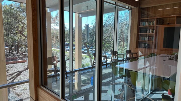 Modern conference room with large glass windows, wooden shelves, and a view of trees an...